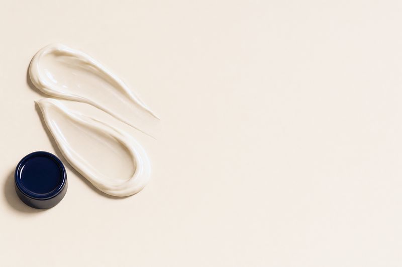 Two swipes of ivory face cream beside a navy jar lid