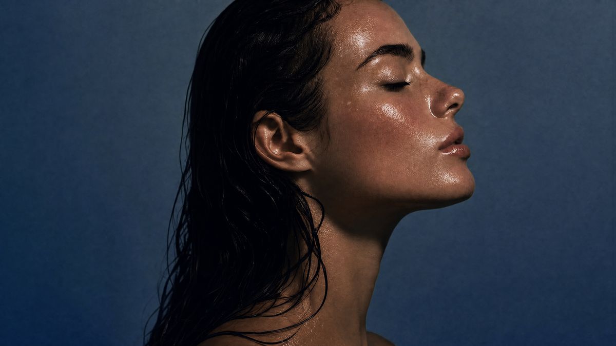 Woman in profile with dewy, glowing skin against a deep blue backdrop